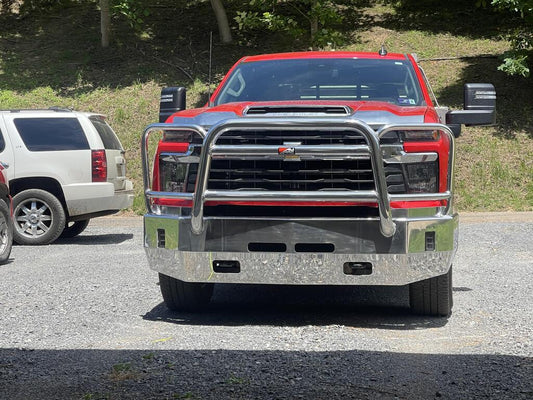 A red truck parked in a truck lot, highlighting a 2024 Chevy Silverado 2500/3500 aluminum front bumper with light cutouts.